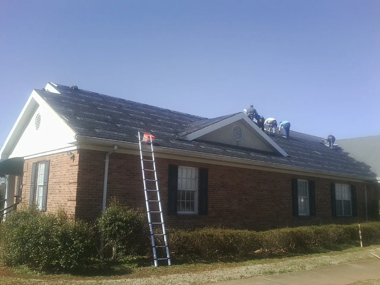 Crew tearing shingles off a brick ranch roof with a ladder set — Metal Roof Repair work by our crew in Sterling